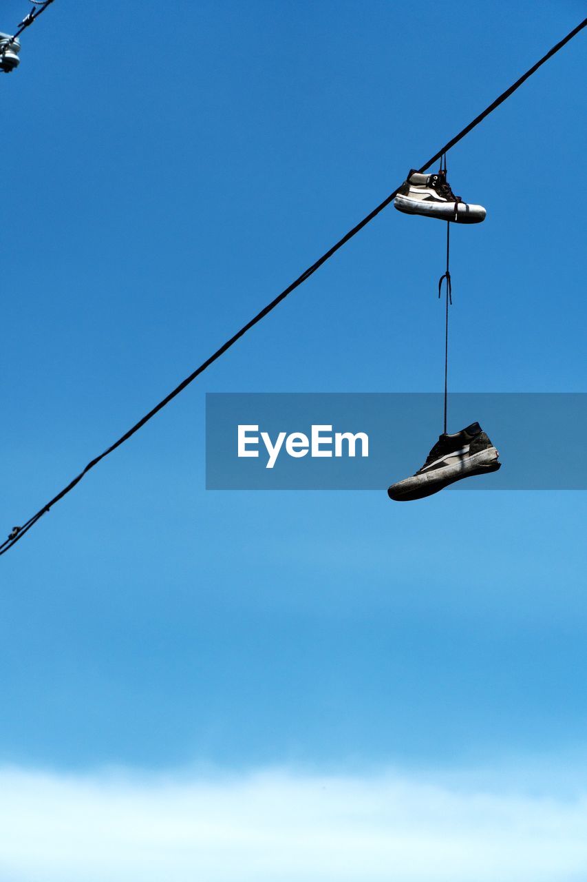 Low angle view of shoes hanging on cable against clear blue sky