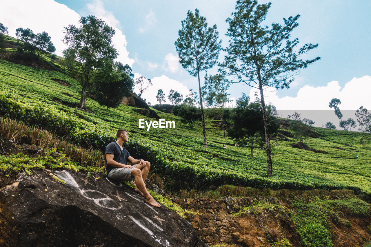 Man sitting on rock at mountain against sky