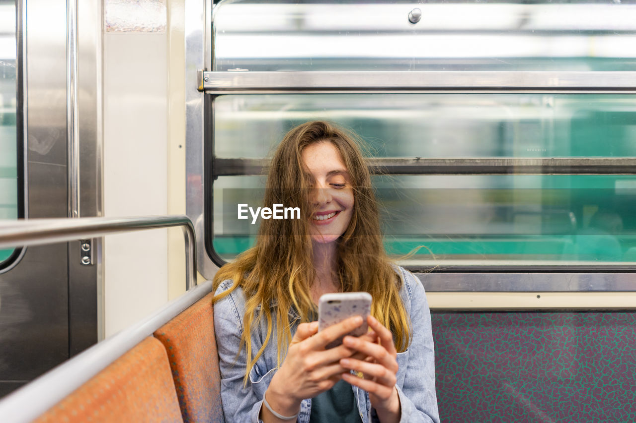 Portrait of smiling young woman in underground train looking at smartphone