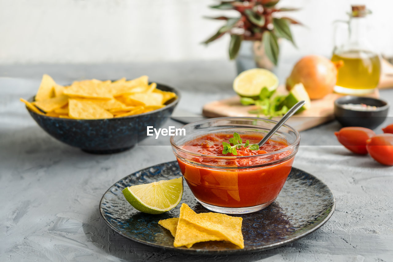 Tomato dip with nachos tortilla in bowl and basic ingredients aside