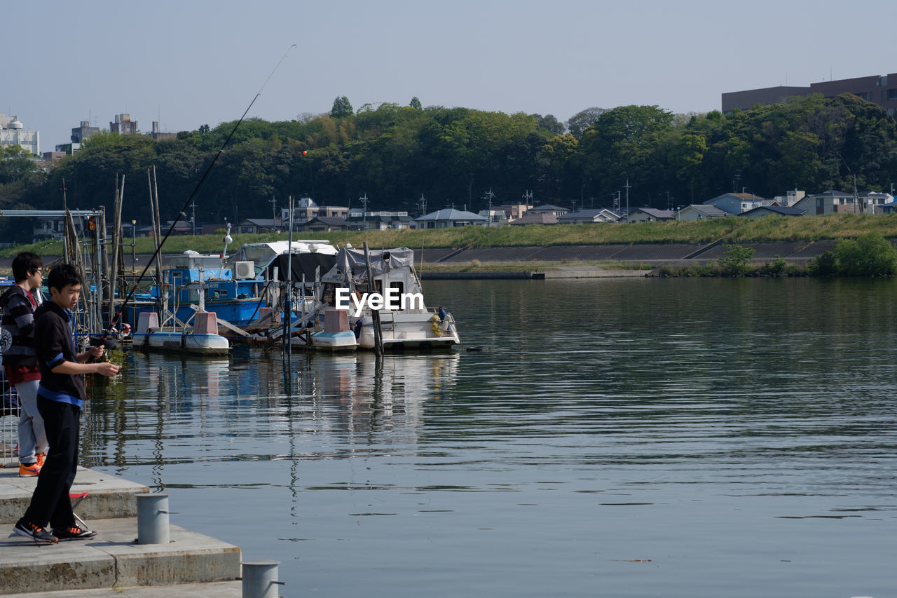 MAN STANDING ON RIVERBANK AGAINST SKY