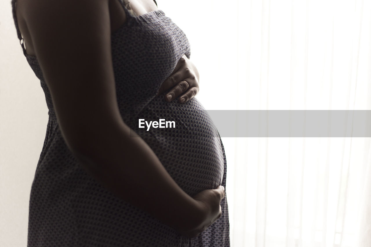 Midsection of pregnant woman touching abdomen against white background