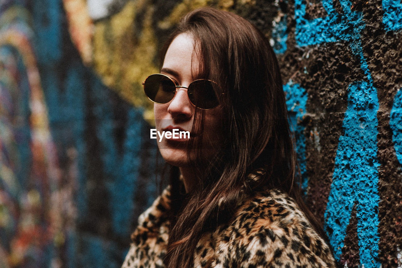 Portrait of young woman wearing sunglasses against graffiti wall