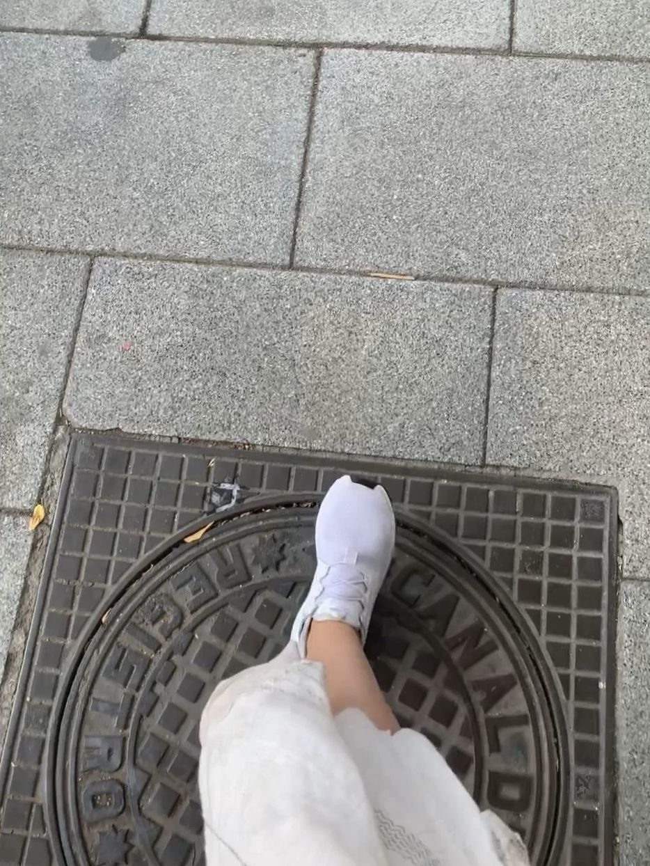 low section, one person, floor, human leg, high angle view, flooring, personal perspective, footpath, shoe, lifestyles, street, day, directly above, city, standing, human limb, human foot, limb, adult, leisure activity, road surface, tile, women, tiled floor, men, casual clothing, white, sidewalk, manhole, paving stone, outdoors, wall