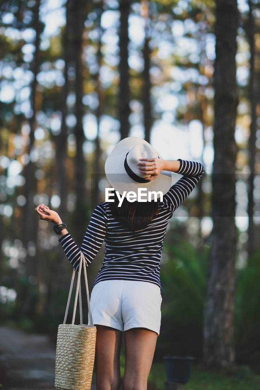 Rear view of woman in hat standing against trees