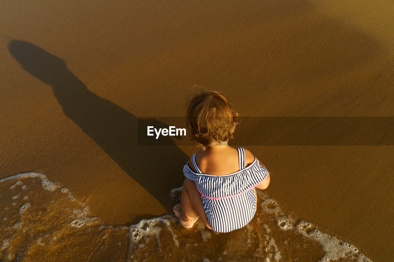 High angle view of cute girl crouching on sand at beach