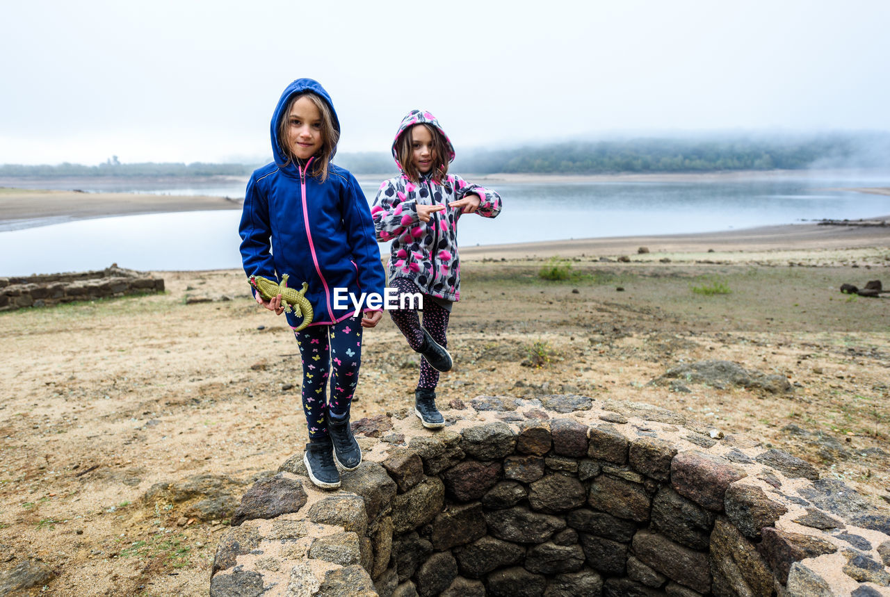 Portrait of sisters standing on water well against sky