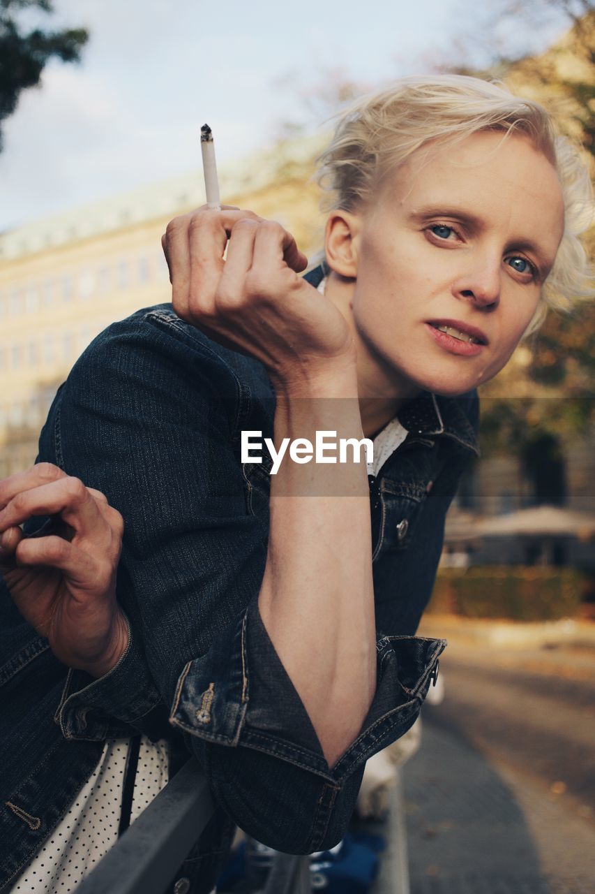 Mid adult woman holding cigarette while leaning on railing 