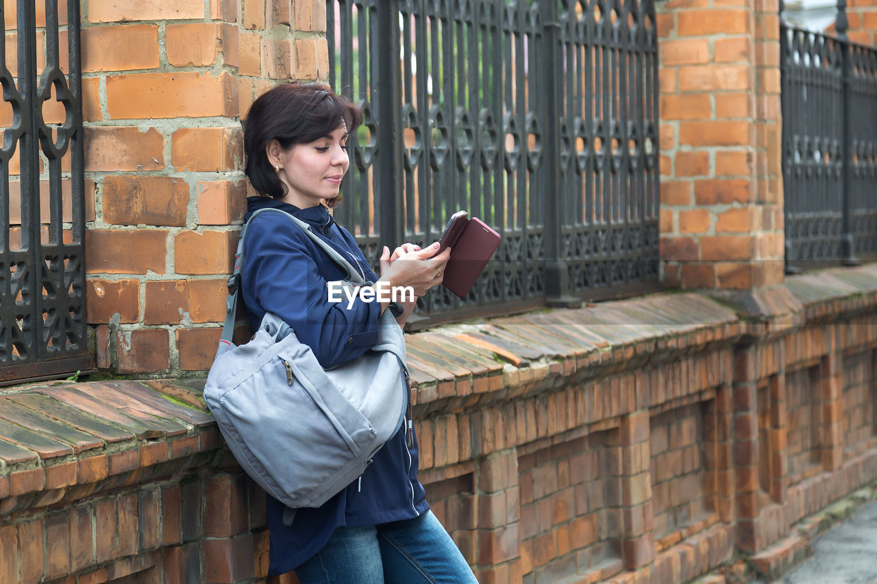 A brunette woman on the street with a smile looks into the phone texting with her lover.