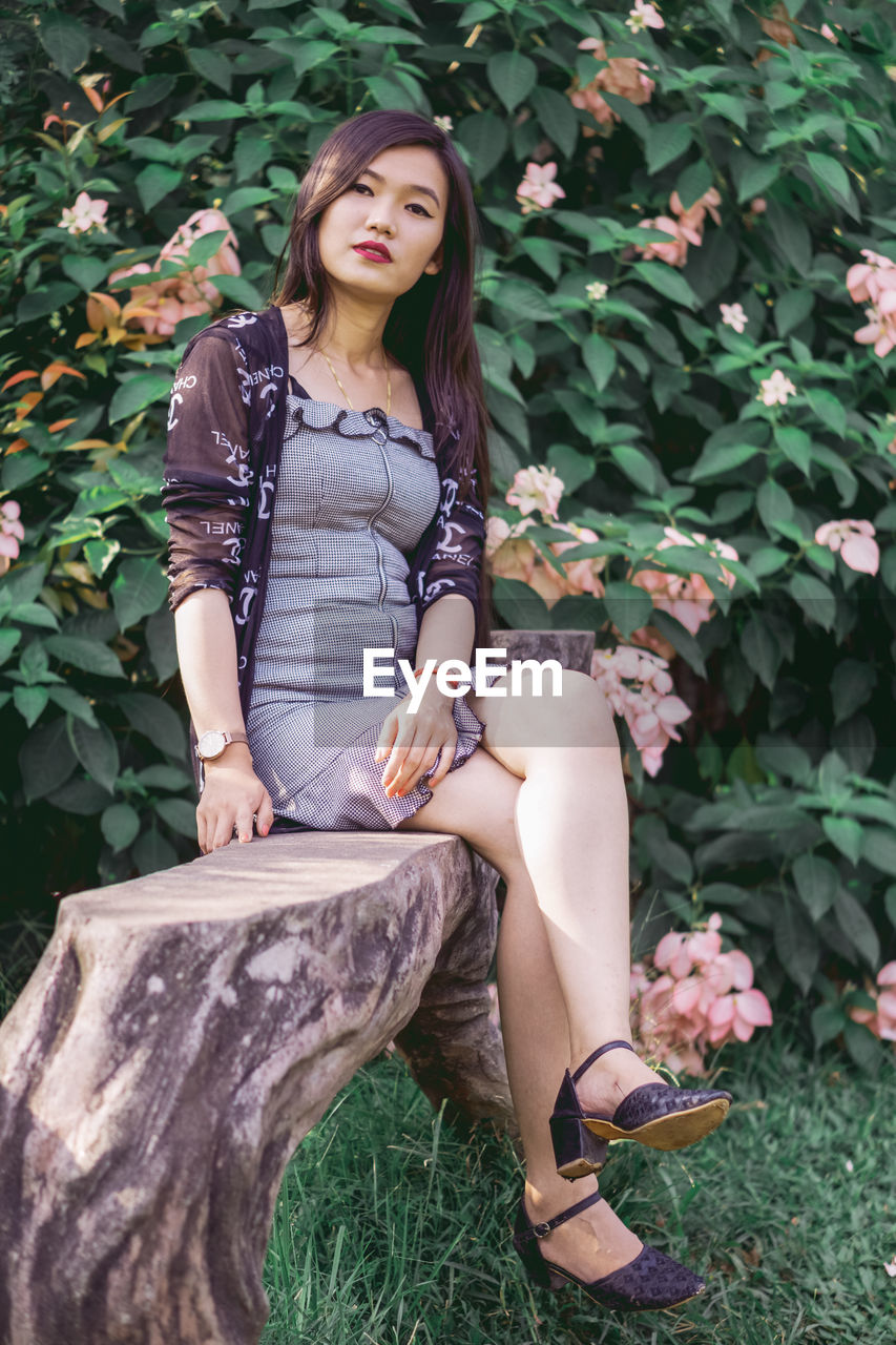 Portrait of young woman sitting against plants 