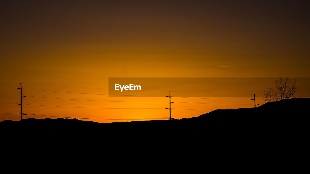 SILHOUETTE OF ELECTRICITY PYLON AGAINST SKY DURING SUNSET