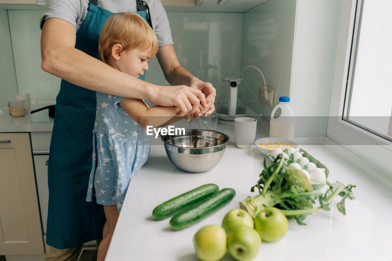 Mom teaches her little daughter how to cook dinner.