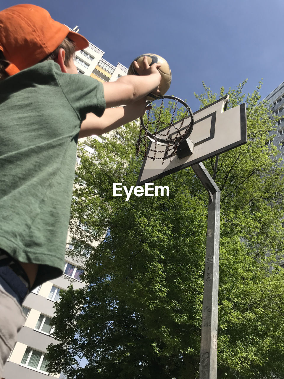 Low angle view of boy playing basketball against sky during sunny day