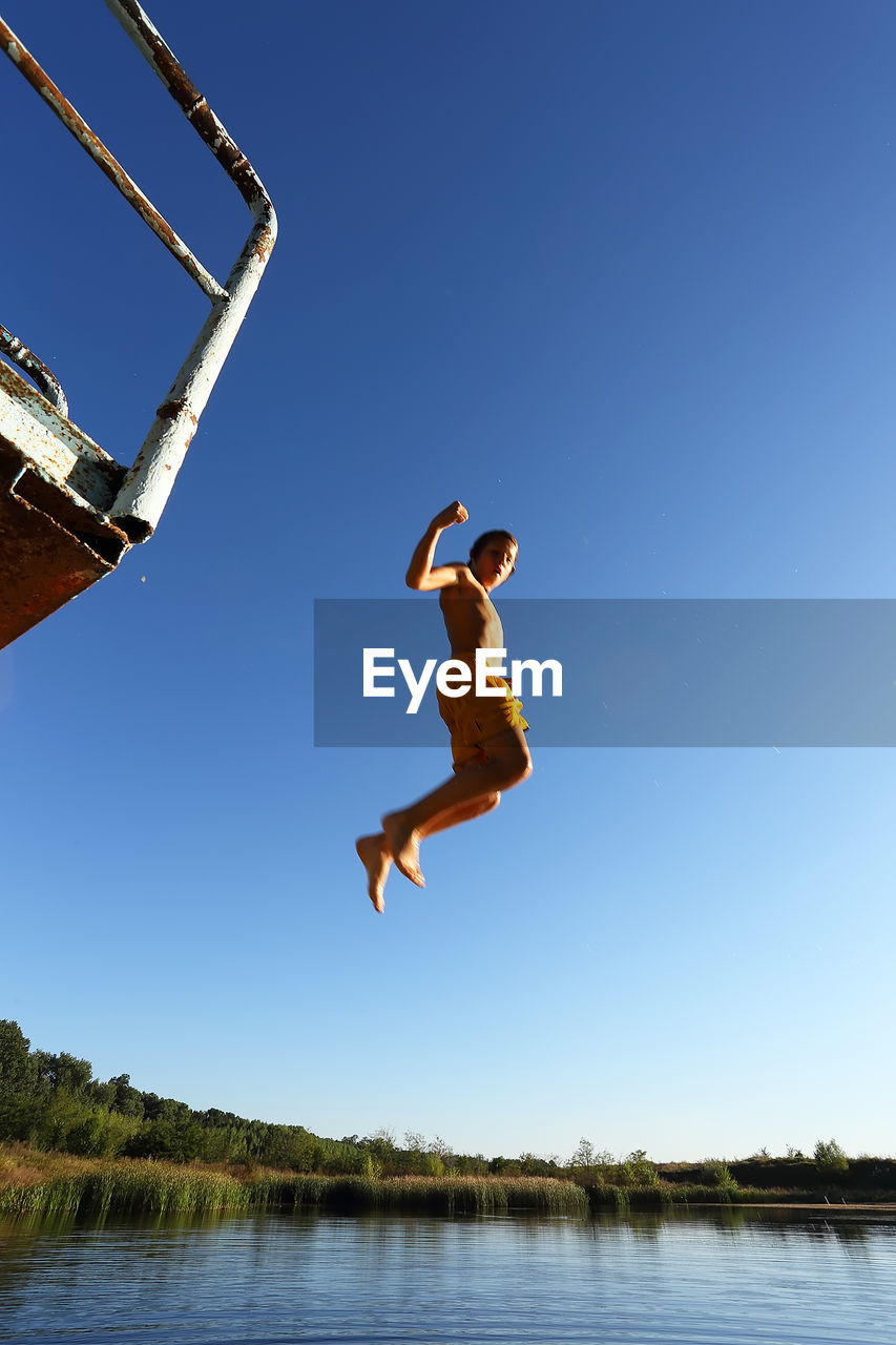 FULL LENGTH OF MAN JUMPING AGAINST CLEAR BLUE SKY