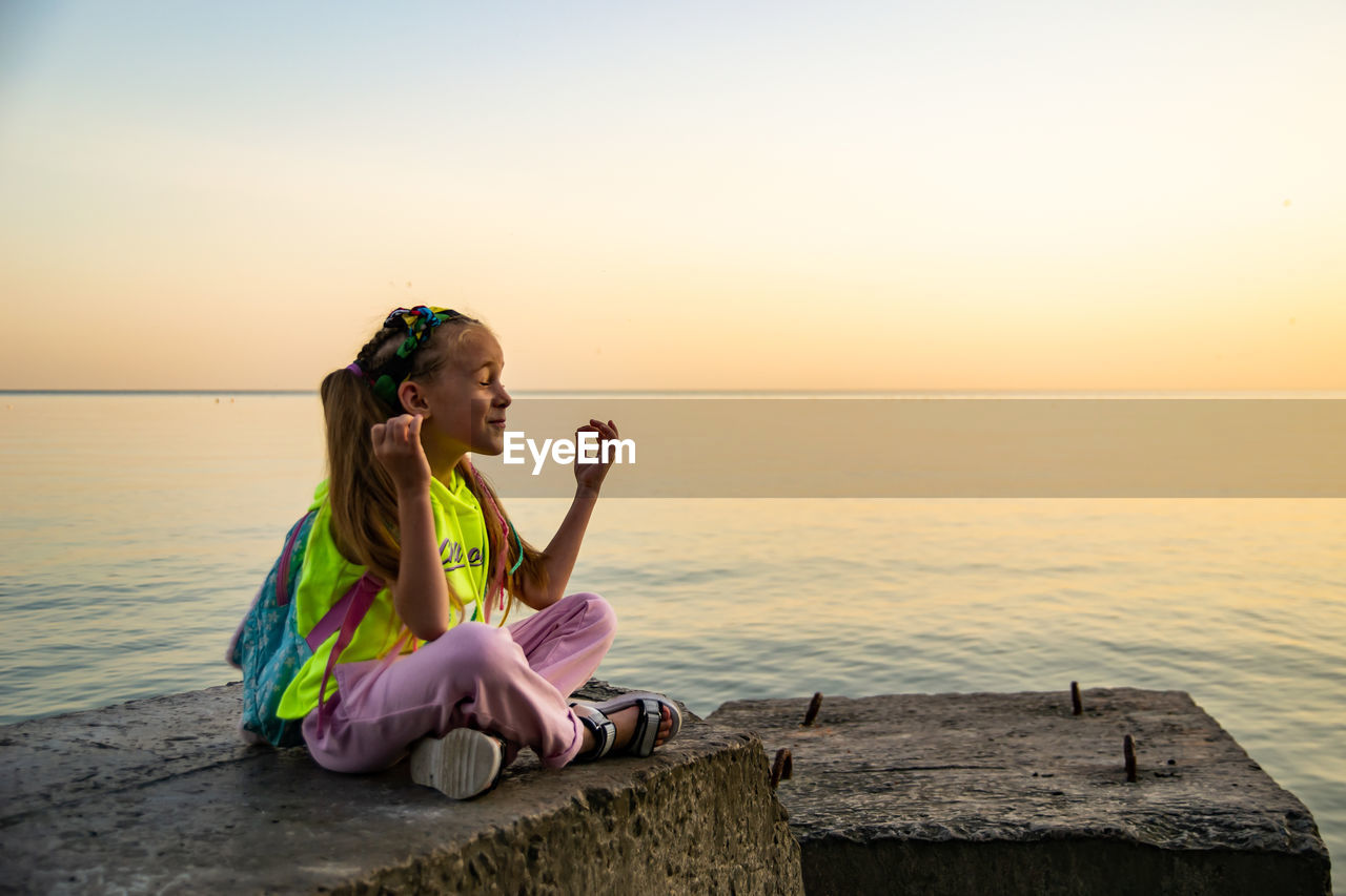 Boy sitting on shore against sea during sunset