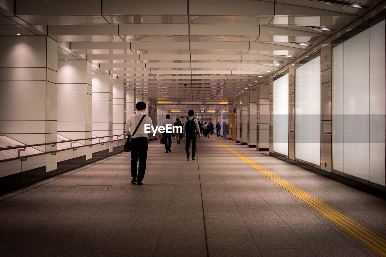 REAR VIEW OF PEOPLE WALKING IN CORRIDOR OF BUILDING