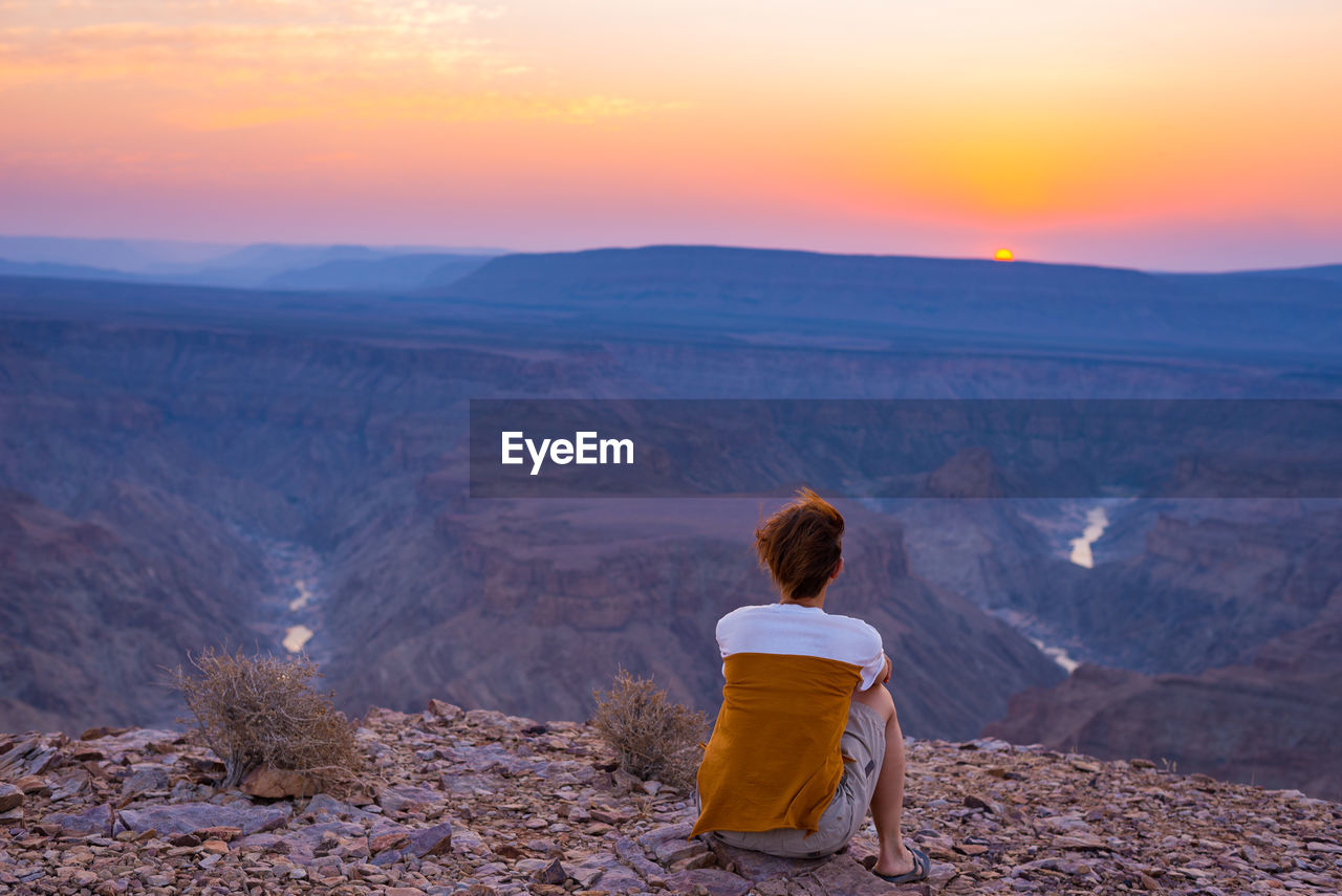 Rear view of tourist sitting on rock at namib-naukluft national park