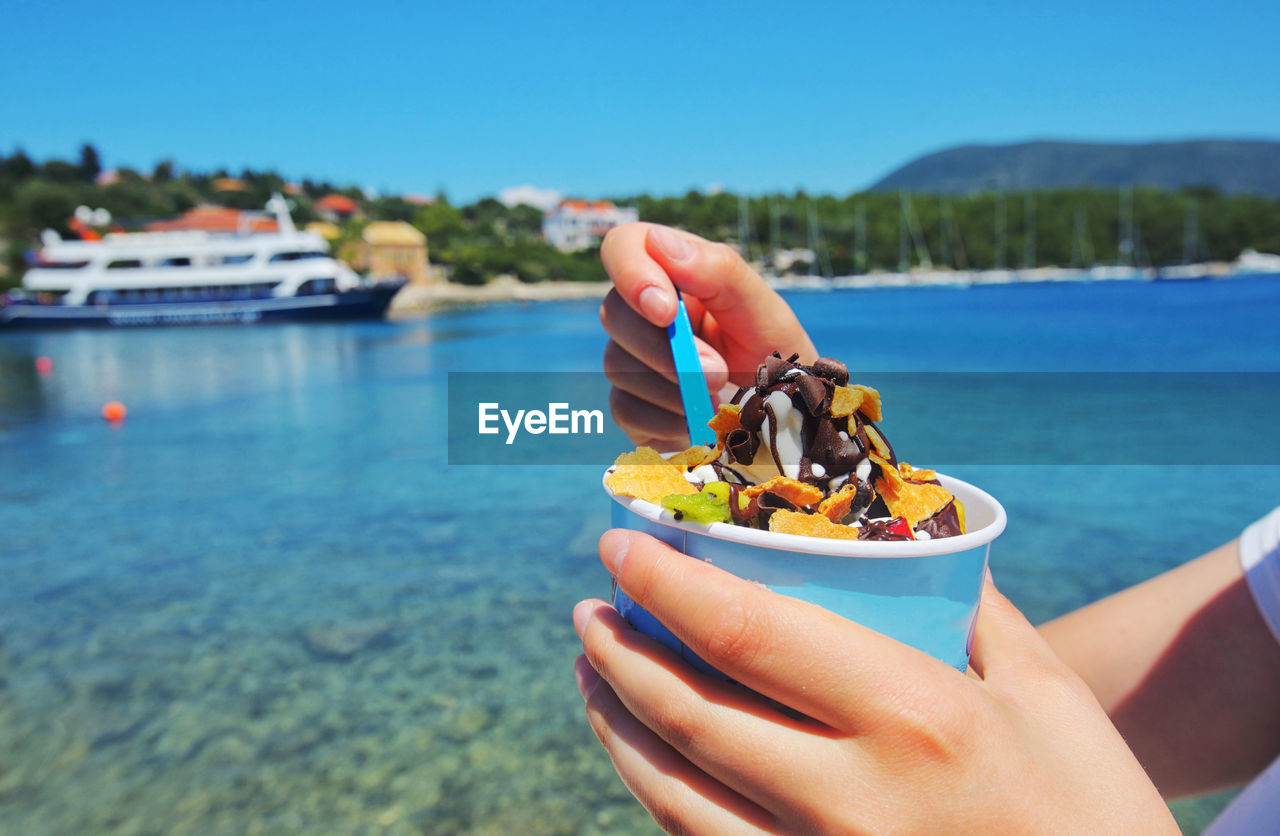 Midsection of woman holding ice cream sundae in container by sea