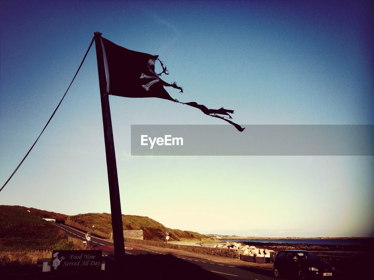 Torn pirate flag on pole on the side of a seaside road