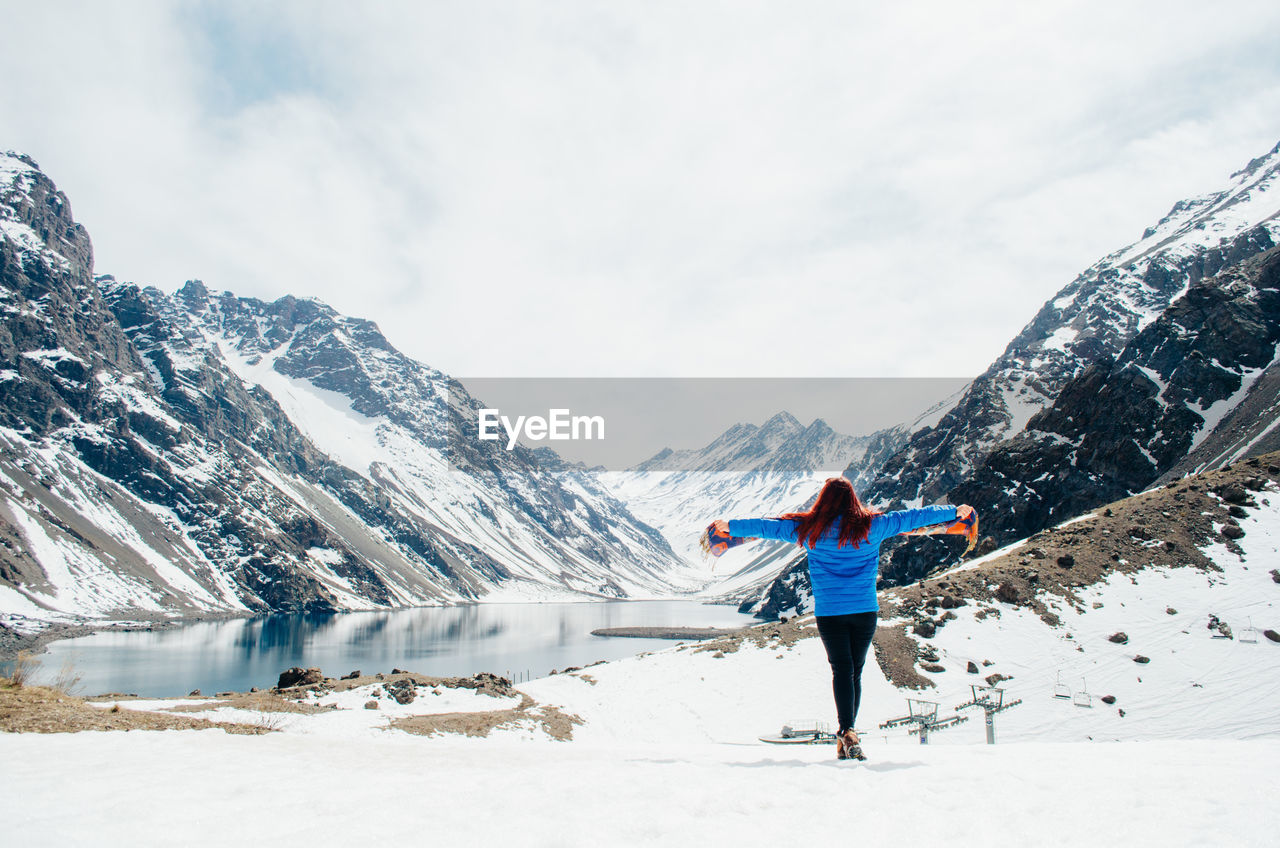 Full length of woman standing by lake against snowcapped mountain