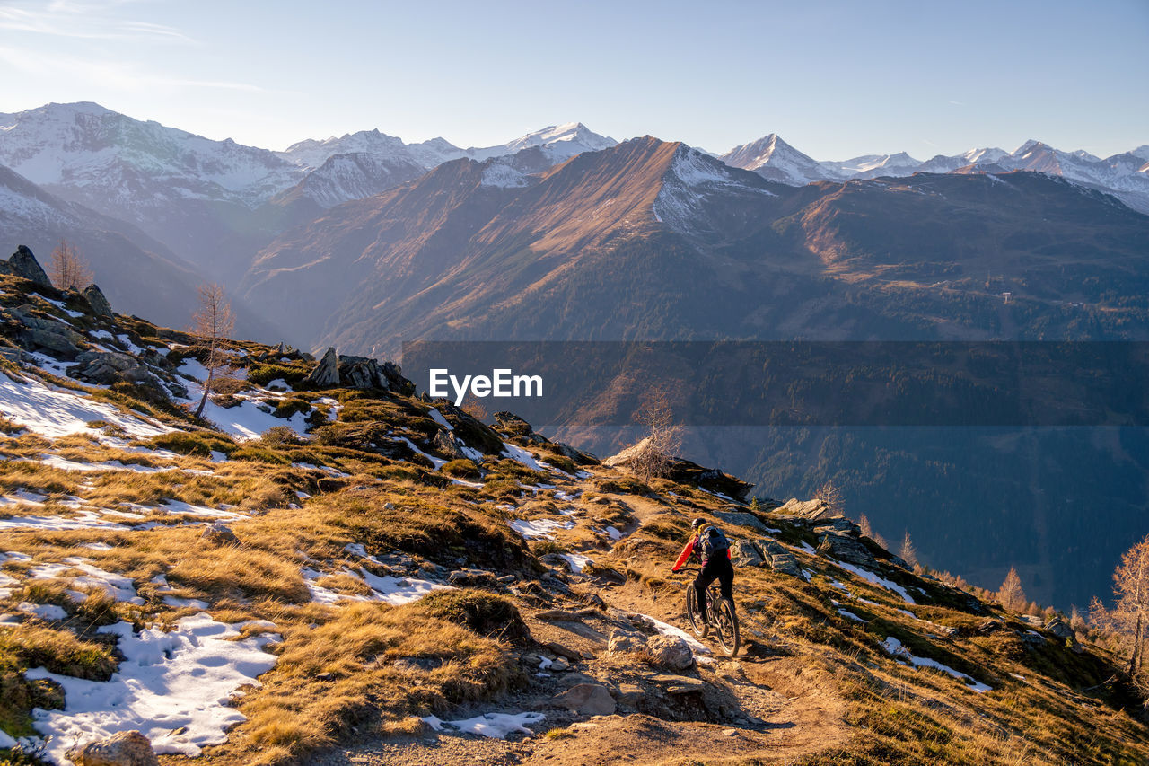 Woman riding a mountain bike on footpath in snow covered alpine terrain, gastein, salzburg, austria.