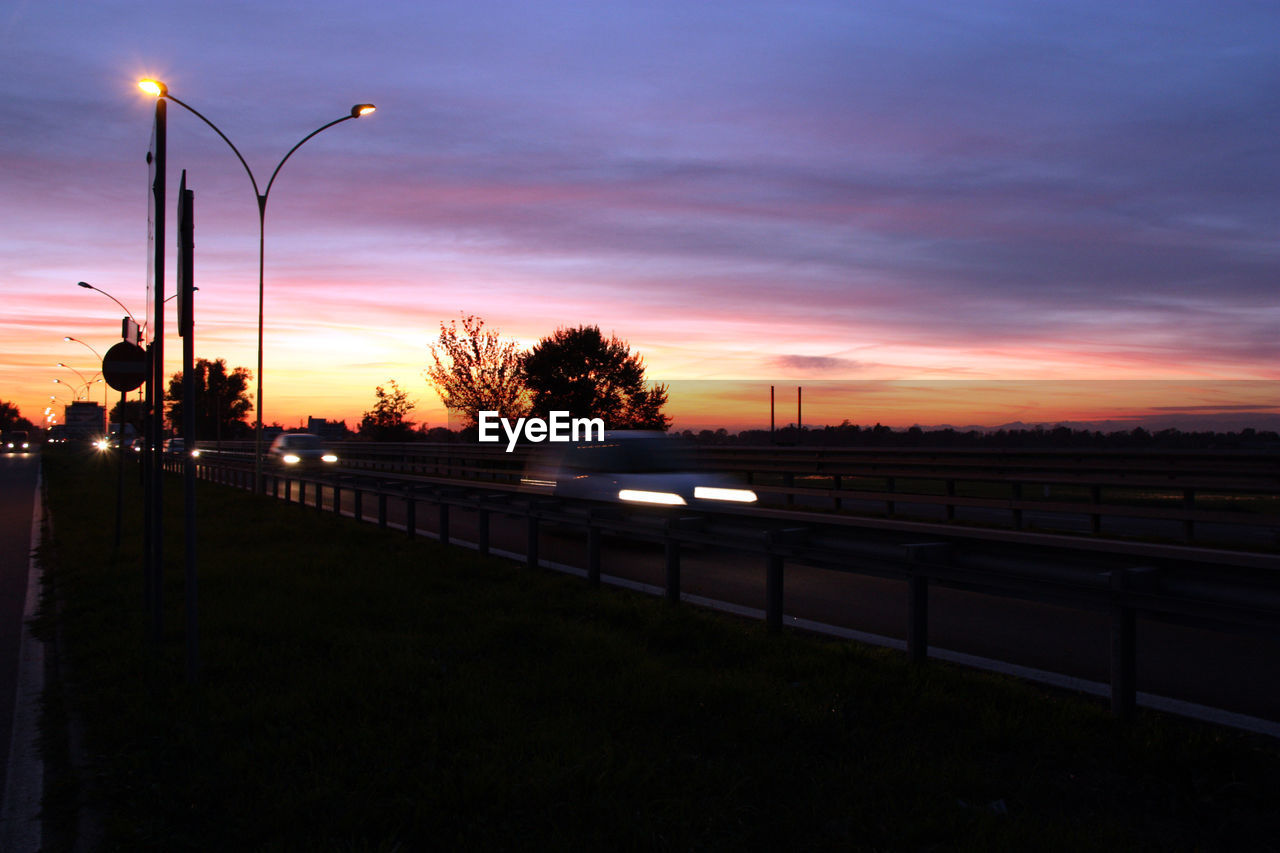 VEHICLES ON ROAD AGAINST SCENIC SKY