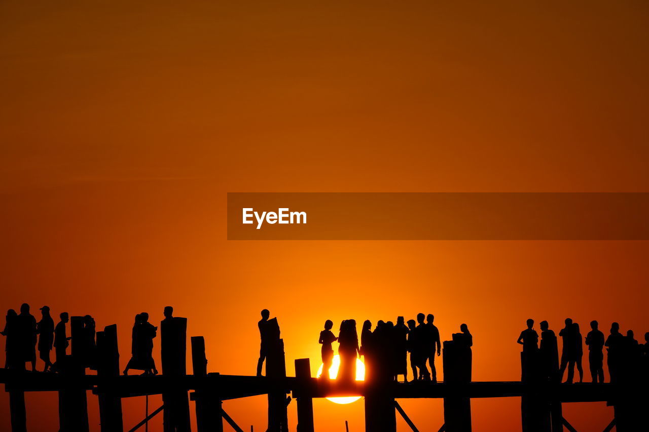 Silhouette people standing on pier against orange sky