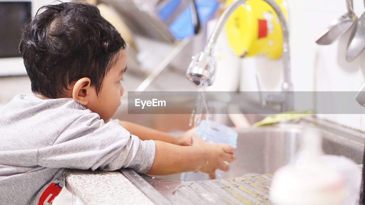 Rear view of boy drinking water from faucet