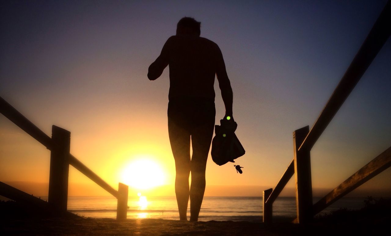 Silhouette person walking on beach at sunset