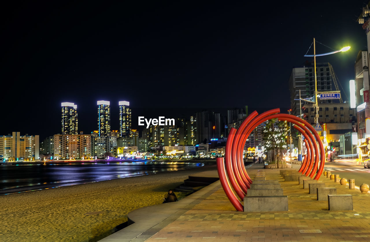 ILLUMINATED MODERN BUILDINGS BY RIVER AGAINST SKY AT NIGHT