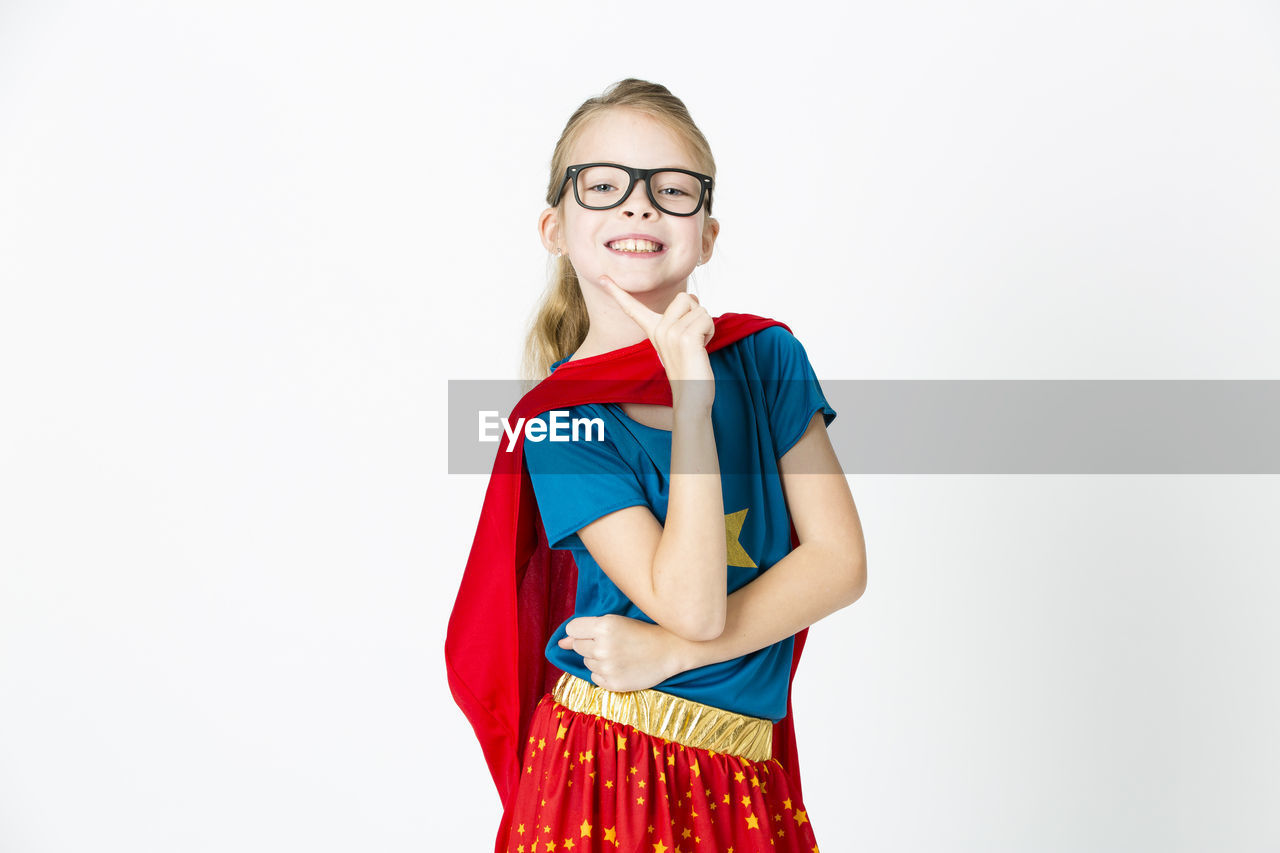 Cute playful girl wearing red cape standing against white background