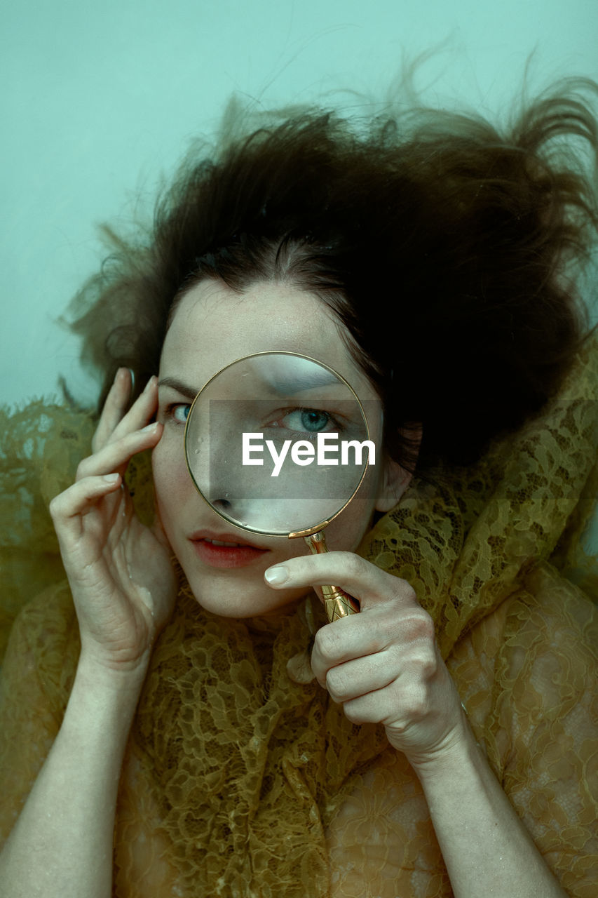 Close-up waterportrait of young woman holding a magnifier 