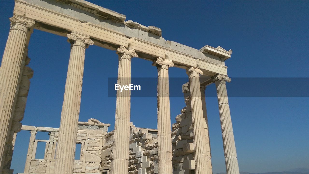 Low angle view of old ruins at acropolis against clear blue sky