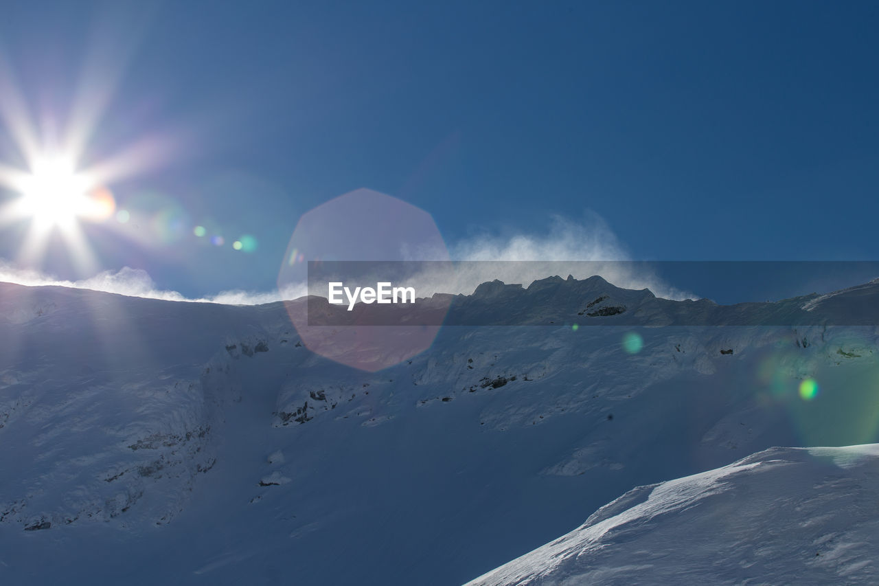 SCENIC VIEW OF SNOWCAPPED MOUNTAINS AGAINST BRIGHT SUN