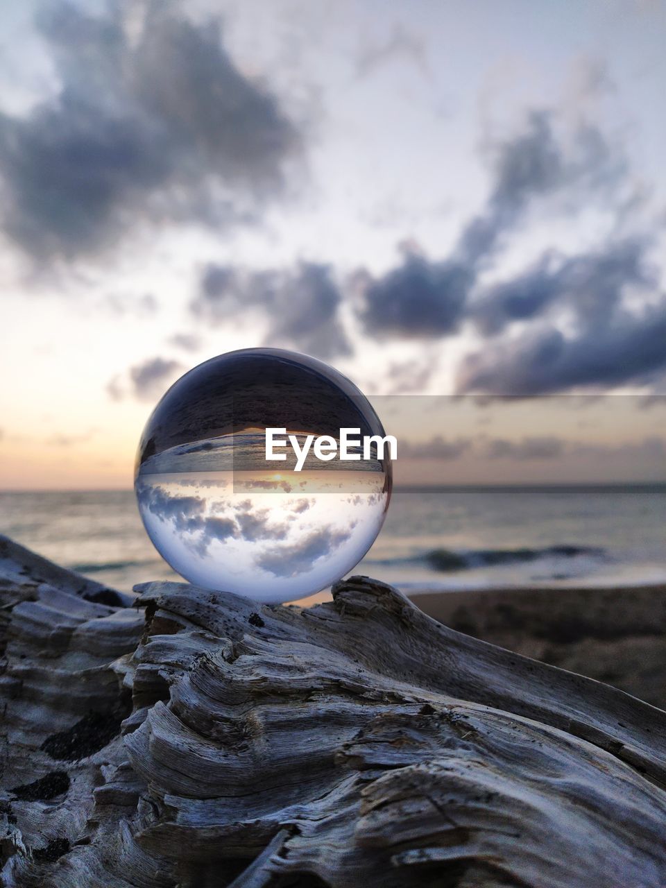 CLOSE-UP OF CRYSTAL BALL ON BEACH AGAINST SUNSET SKY