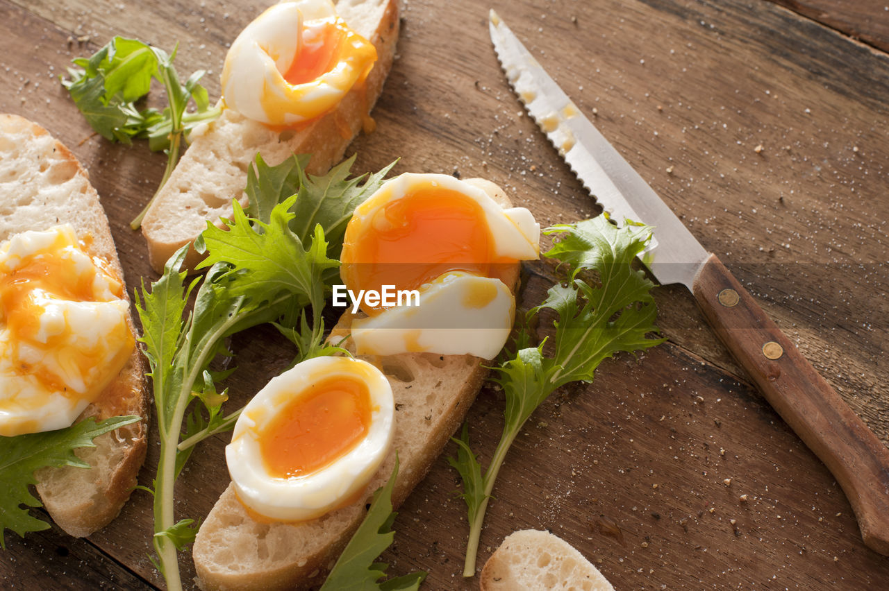 Tasty soft boiled eggs and salad greens on sliced fresh white bread with a kitchen knife on a table