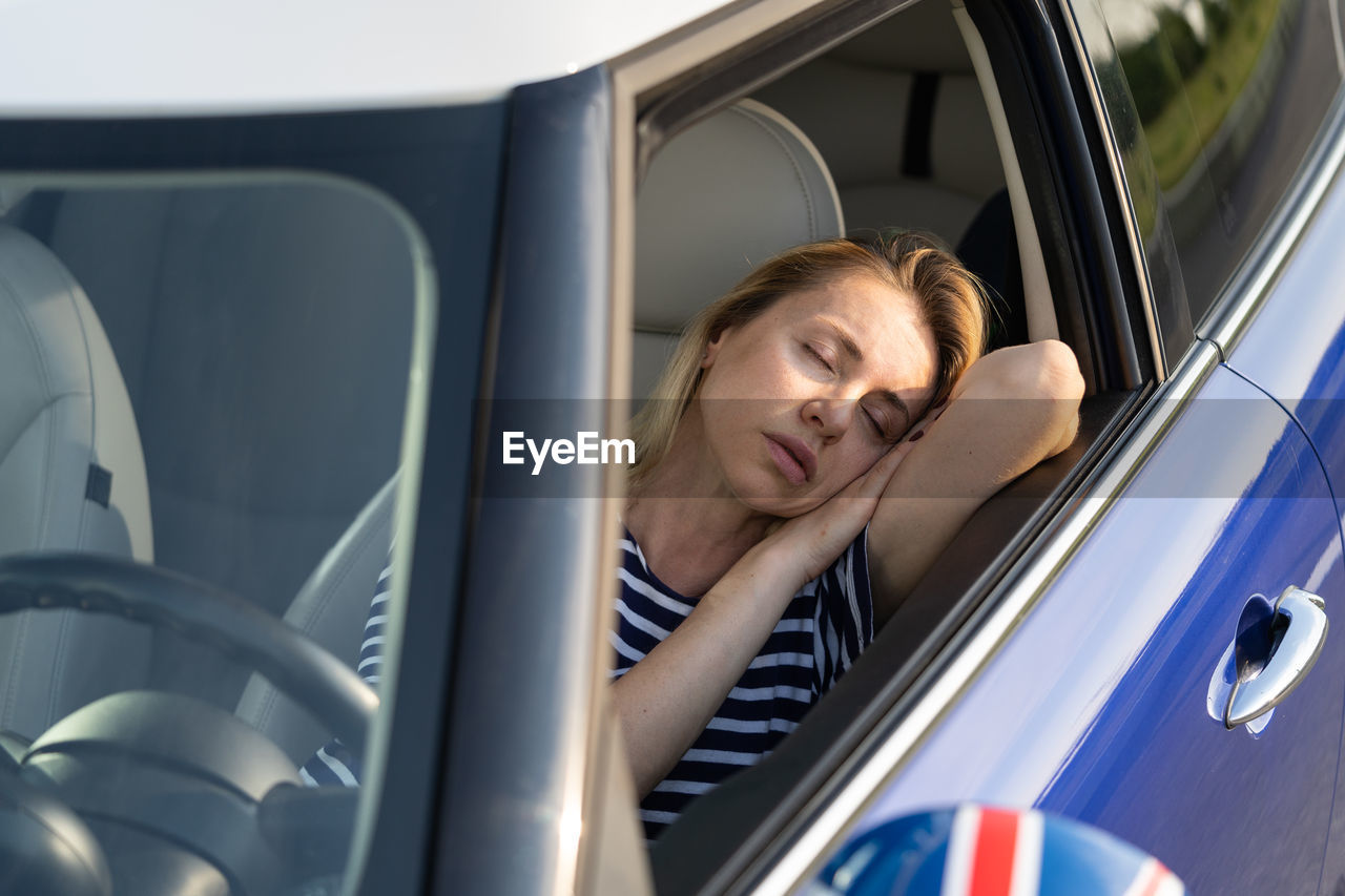 Woman tired of driving sleep on front seat. female travel by car on road trip resting napping inside