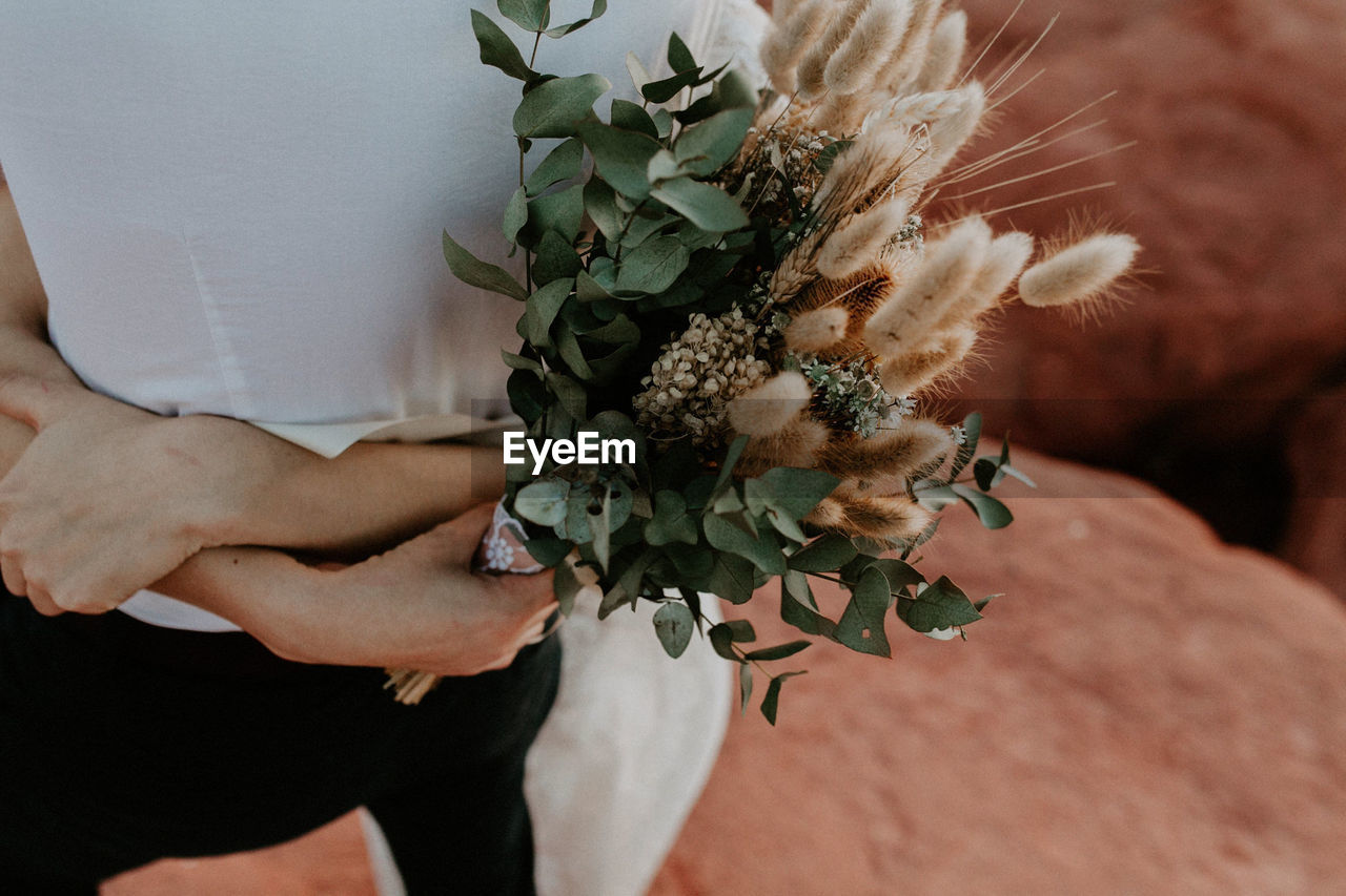 Cropped image of bride holding bouquet while embracing groom