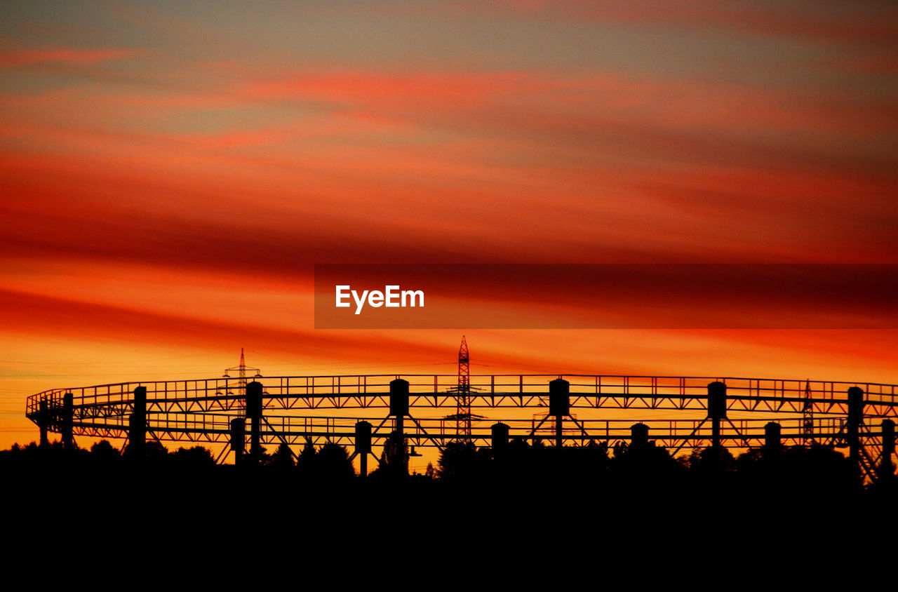 Silhouette electricity pylons against dramatic sky during sunset