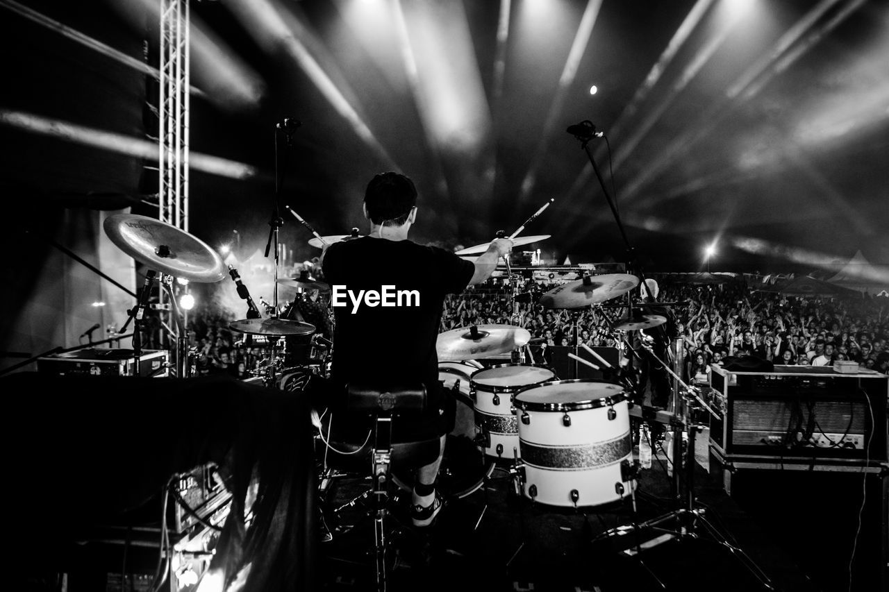 Rear view of drummer playing drums against crowd at music concert