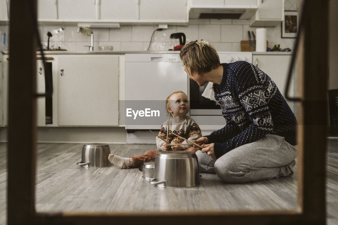 Girl looking at mother while playing utensils with chopsticks in kitchen at home