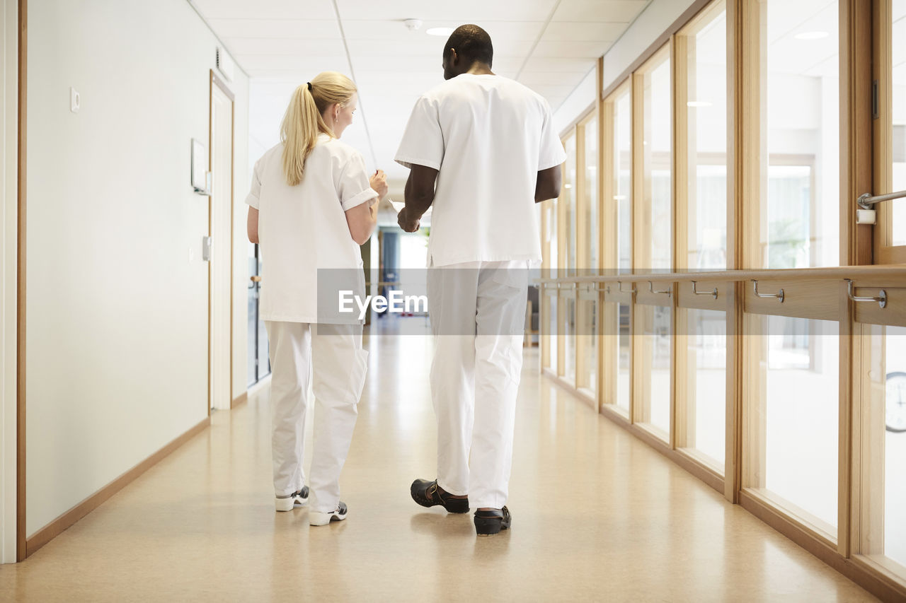 Full length rear view of male and female nurse walking in hospital corridor