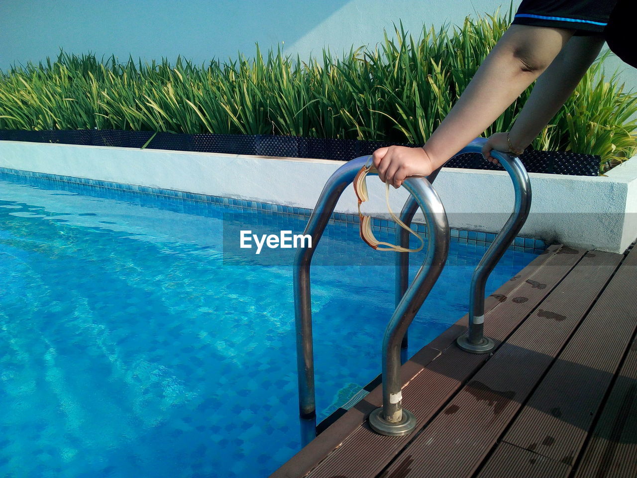 Cropped hands of person holding swimming goggles on ladder of pool