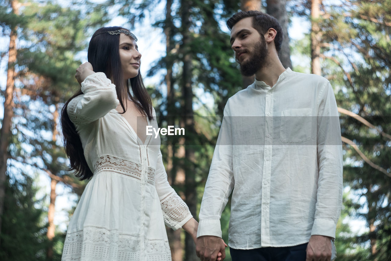 Romantic couple holding hands while standing in forest