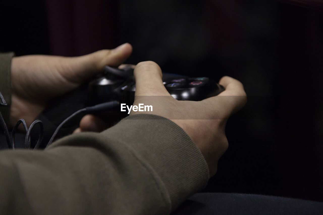 Cropped hands of person playing video game against black background