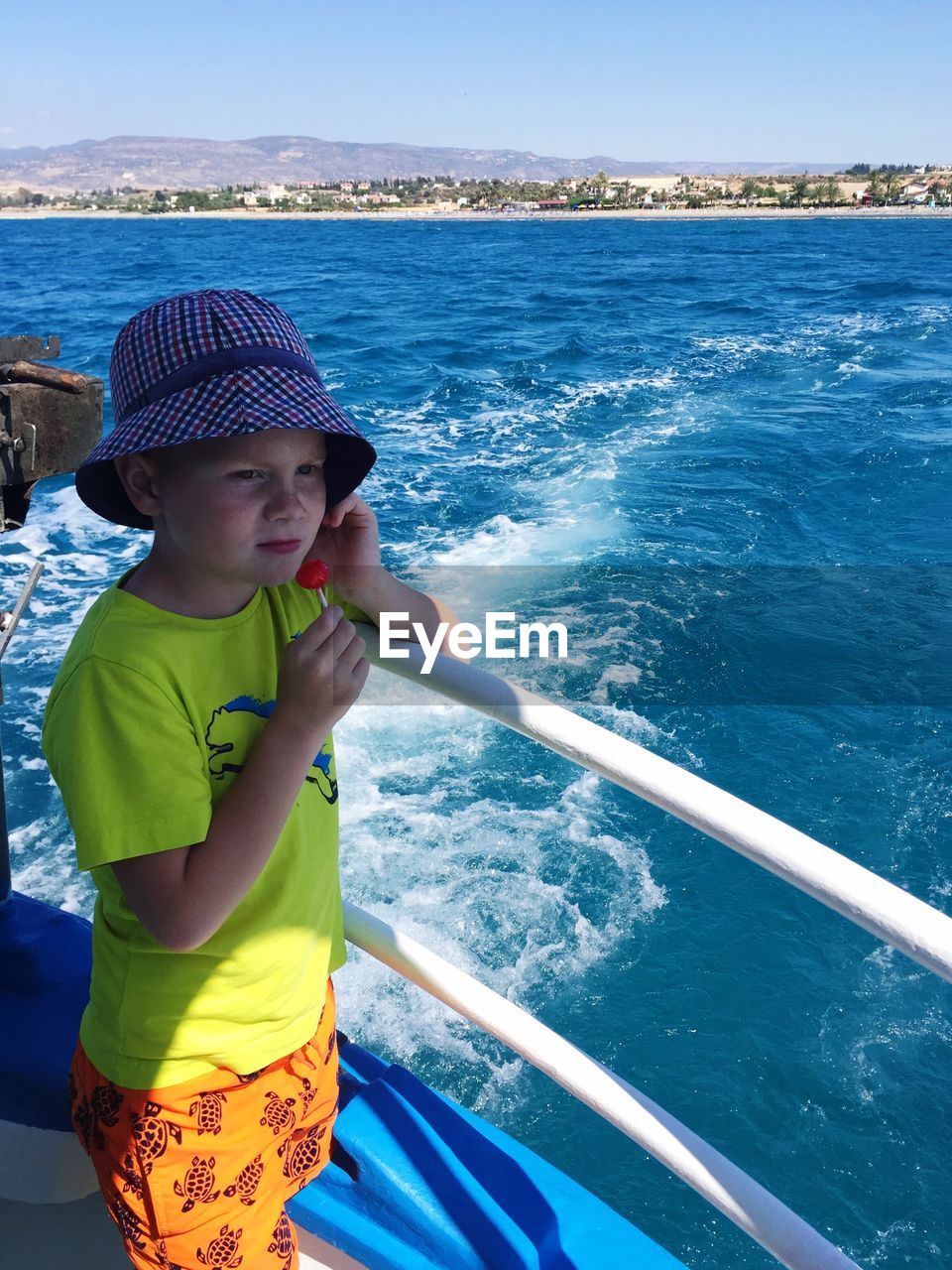 High angle view of boy eating lollipop while standing by railing in boat