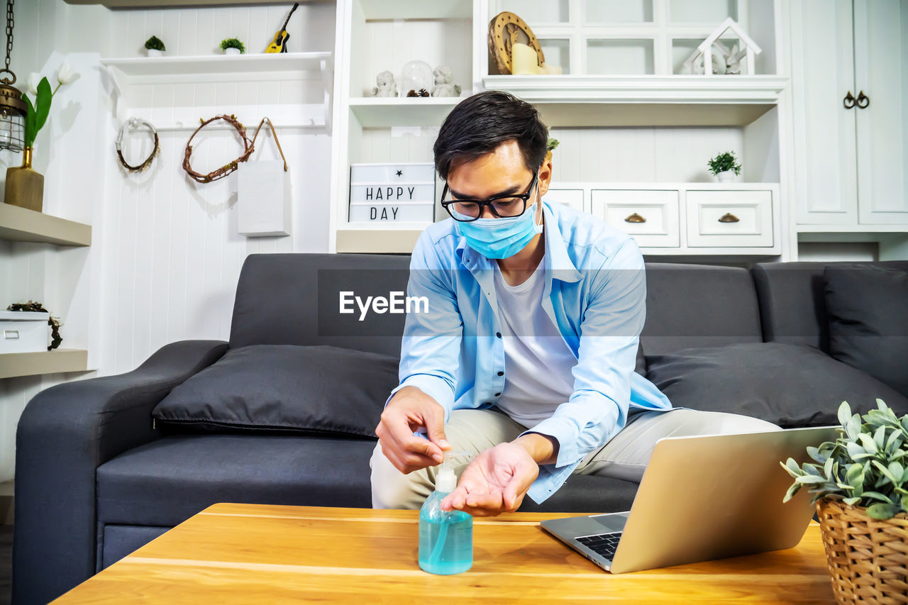 Young man wearing mask using hand sanitizer at home