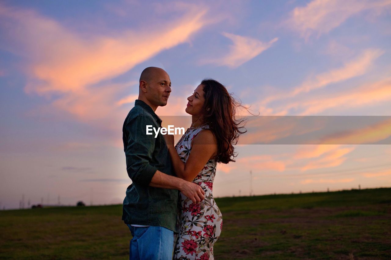 COUPLE STANDING ON FIELD AT SUNSET