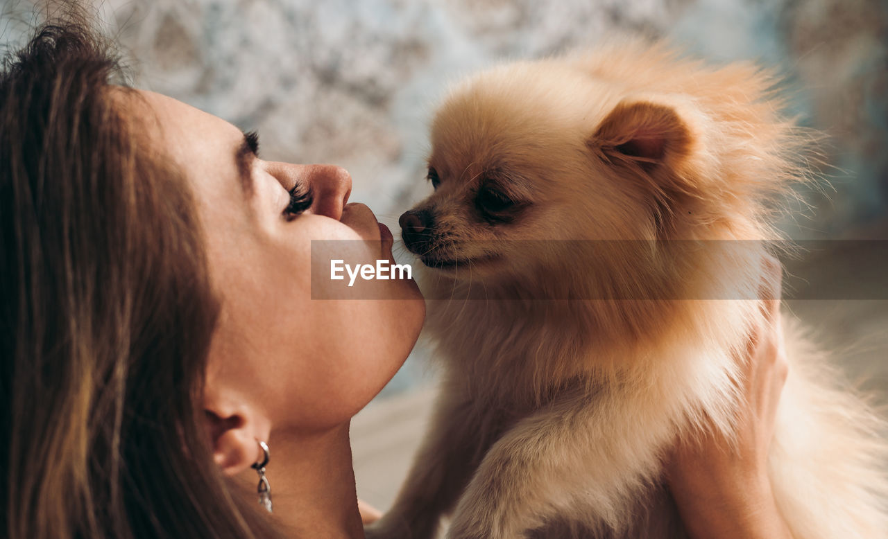 Cute young brunette girl kisses her pomeranian spitz dog. the concept of home comfort and pet care