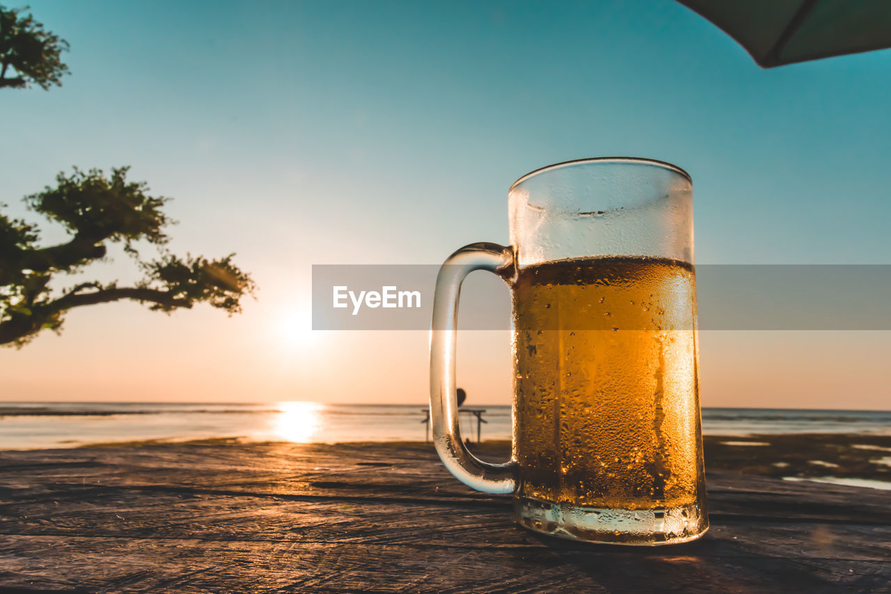 Beer glass on table against sea during sunset